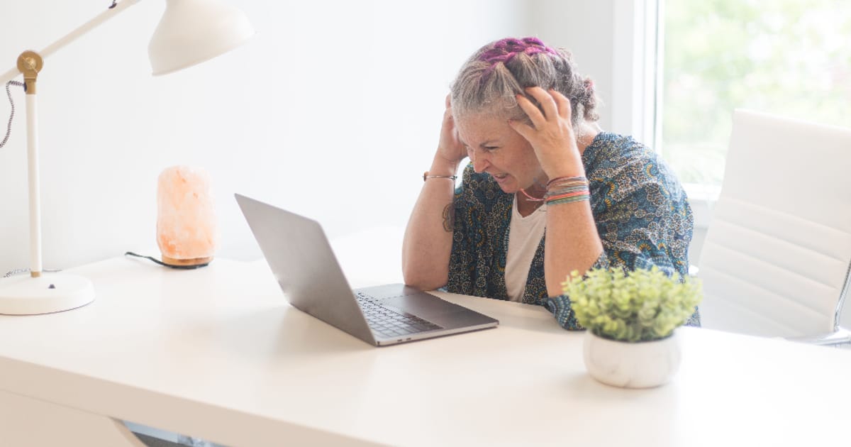 A frustrated person holding their head while working at a laptop